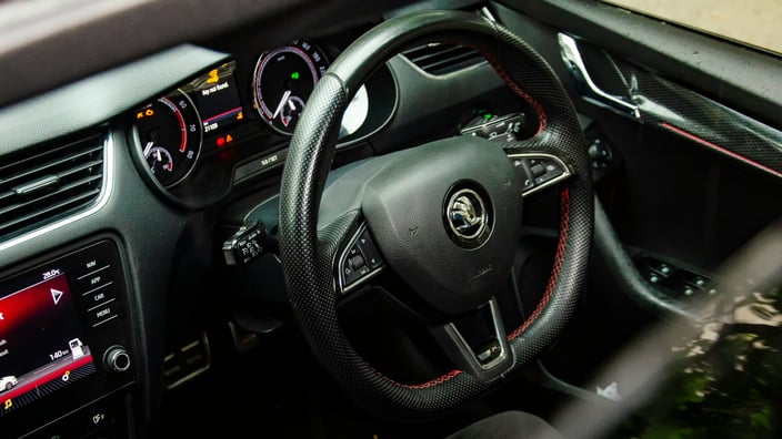 Interiér vozu Škoda se sportovním volantem a rozsvícenou varovnou kontrolkou na palubní desce, která signalizuje potřebu diagnostiky elektroniky.