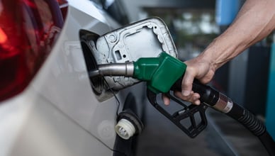 Detailní pohled na ruku držící zelenou tankovací pistoli při doplňování paliva do nádrže bílého automobilu.