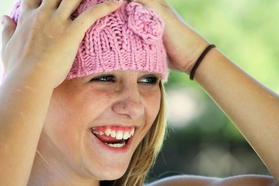 AI teeth whitening filter before photo - woman wearing pink hat smiling in sunlight