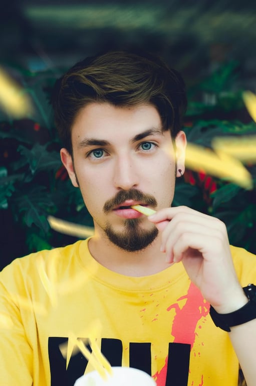 a portrait of a man with a classic goatee style, featuring a neatly trimmed beard on the chin and a mustache, against a solid background