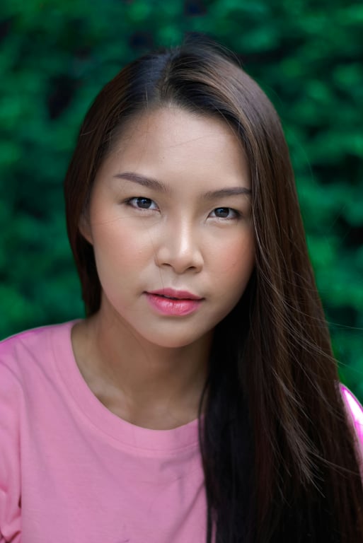 Portrait with natural makeup, pink top, long straight hair, green blurred background.
