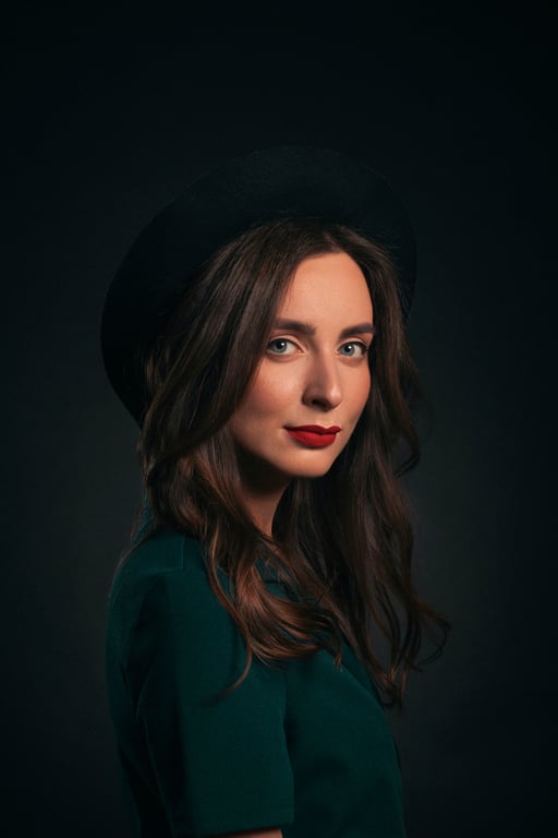 Studio portrait of a woman in a dark green top and black hat.