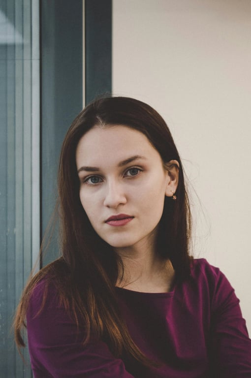 a portrait of a person wearing a minimalist long coat with straight cut, defined shoulder line, fluid inner dress, muted tones, precise tailoring, relaxed posture, soft ambient lighting