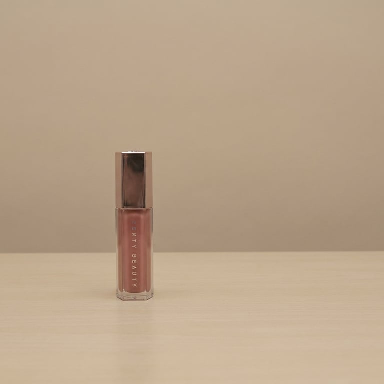 Create an elegant shot of the lipstick on a clean tabletop, alongside a beautiful female model's lips in a soft, sophisticated pose, with a half-body composition and harmonious proportions, set against a light pink studio backdrop, and lit with professional studio lighting that produces gentle, natural shadows for enhanced depth and product emphasis.
