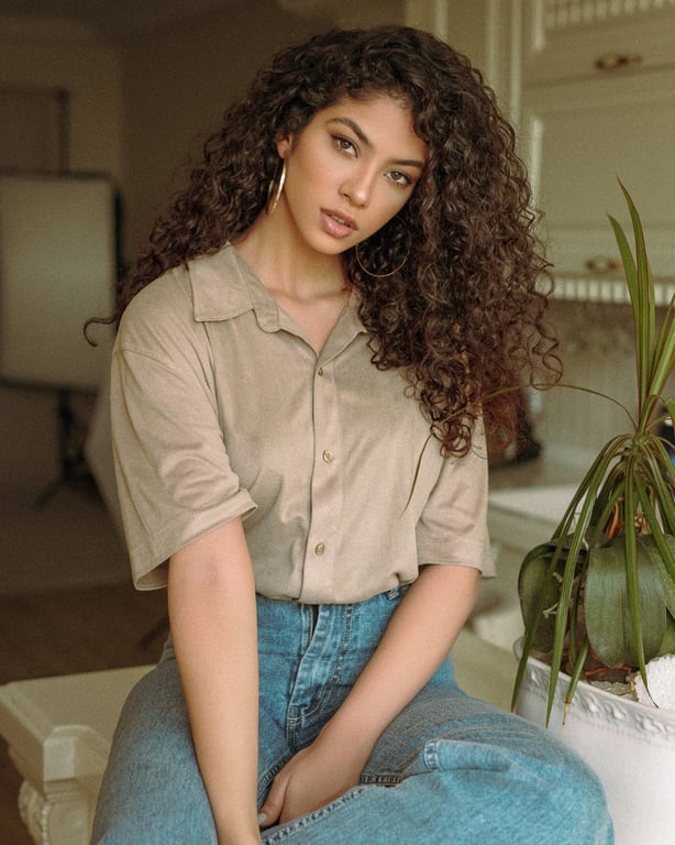 The subject wears a casual beige shirt and denim jeans in a home interior.