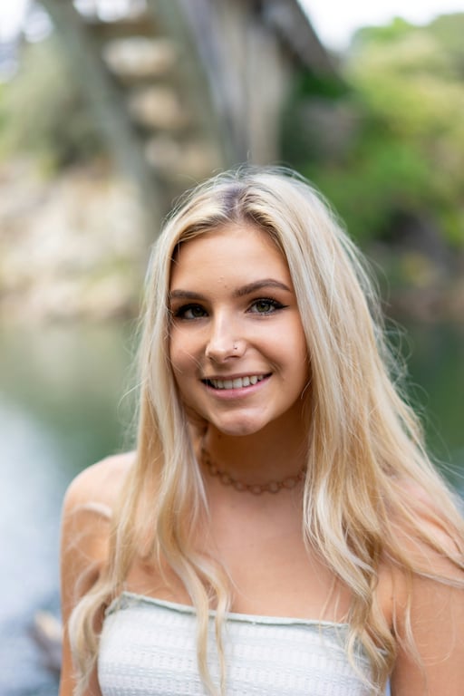 A woman outdoors with long blonde hair smiling near water.