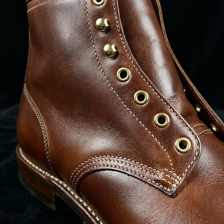 Create a close-up and clean macro shot focusing on the brand new boots’s material, finish, and texture, emphasizing the fine details, subtle reflections, and exquisite surface quality, with a dark, minimalist background that highlights the product's luxurious and sophisticated feel, capturing the way light plays across the smooth, polished surface, showcasing the intricate stitching and premium leather grain.