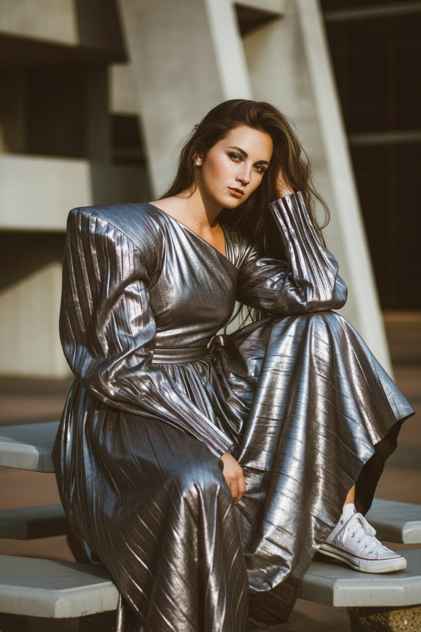 Metallic long gown with strong shoulders, seated outdoors, relaxed pose with white sneakers.
