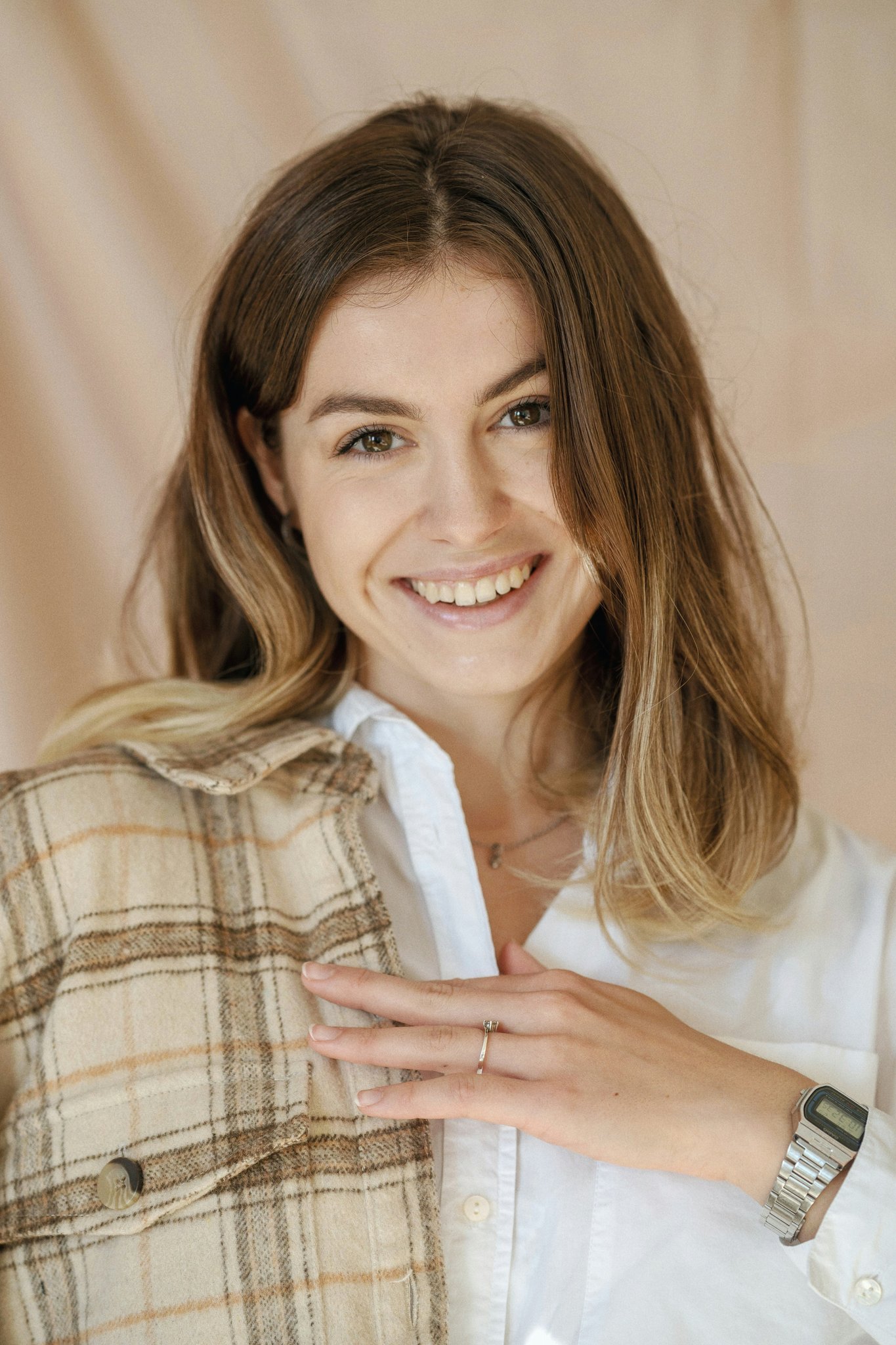 Smiling woman in a plaid jacket and white shirt in front of a soft beige backdrop.