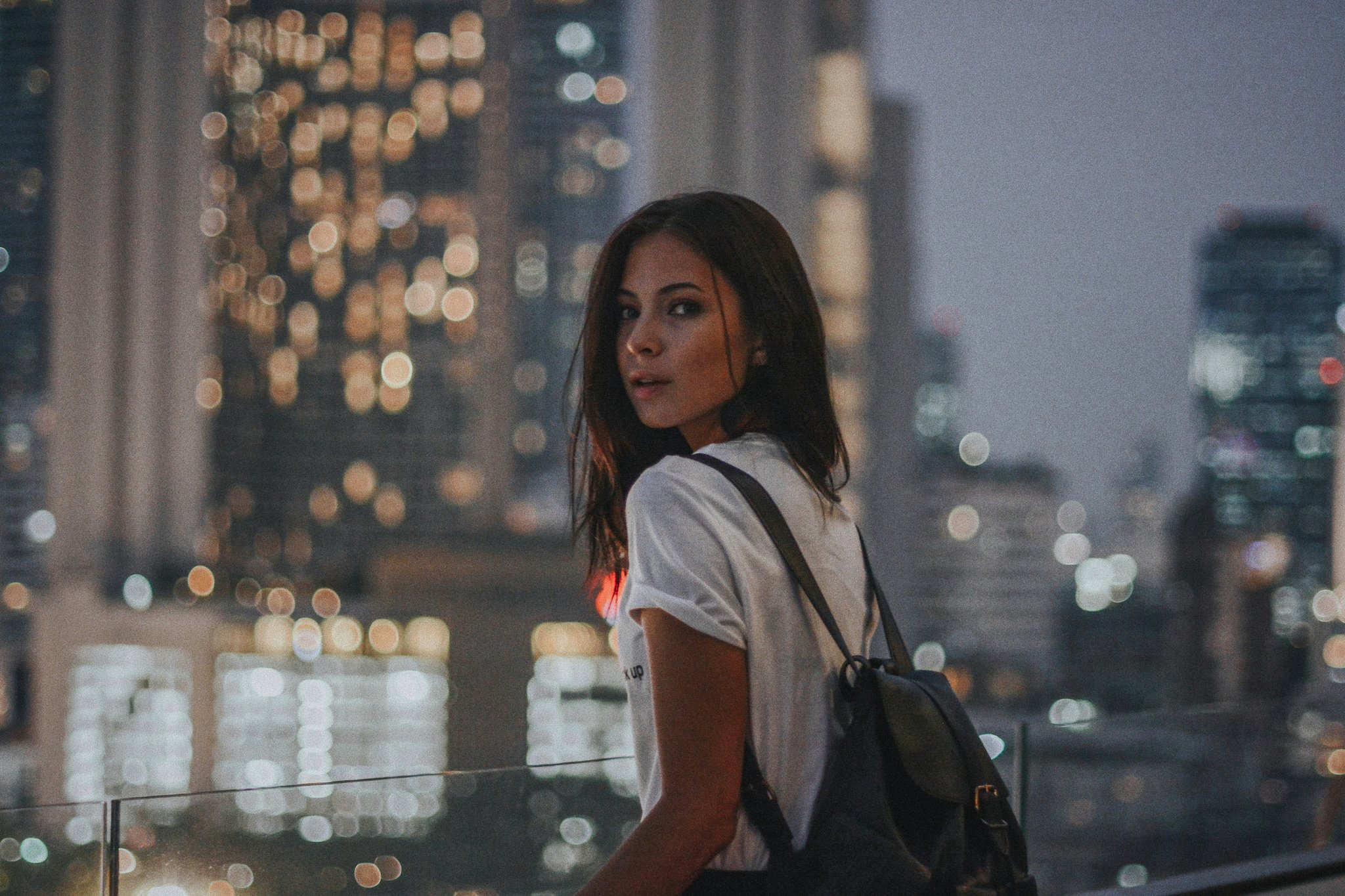 City rooftop scene with soft bokeh lights framing a backpacked figure turning toward the camera.