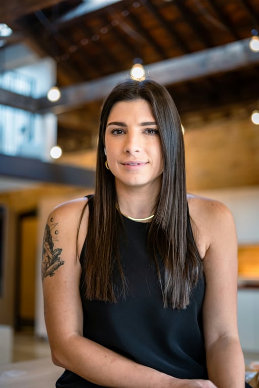 Warm industrial interior framing a calm seated portrait with straight hair and a minimalist black top.