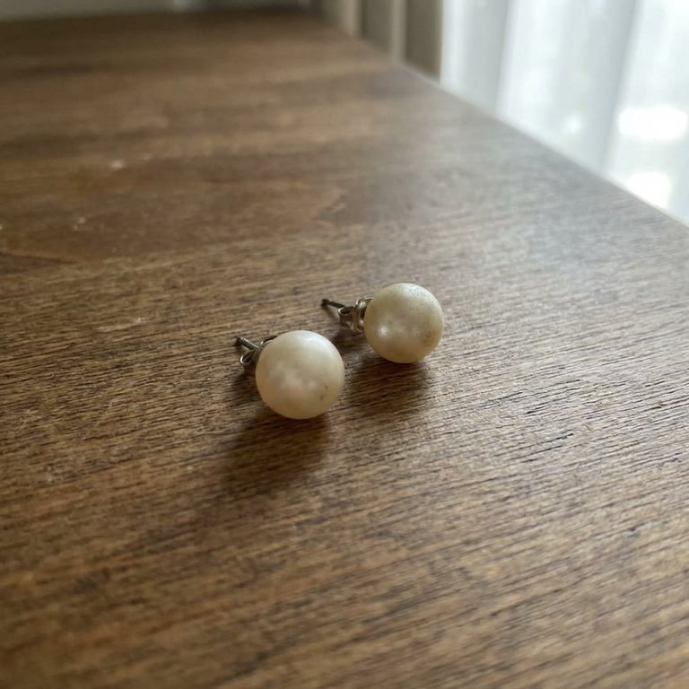 Create a close-up and clean macro shot focusing on the brand new pearl earring’s material, finish, and texture, emphasizing the fine details, subtle reflections, and exquisite surface quality, with a dark, minimalist background that highlights the product's luxurious and sophisticated feel, capturing the way light plays across the smooth, polished surface.