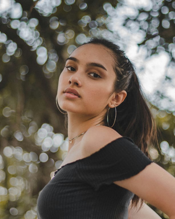 Soft forest bokeh framing a calm profile pose with hoop earrings and natural light.