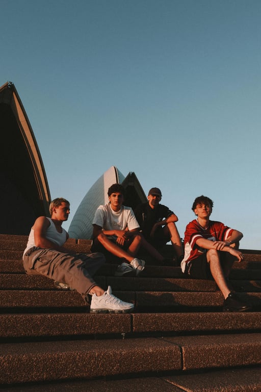 a portrait of multiple young men transformed into a modern K-pop boy group, wearing coordinated stage outfits with tailored jackets, fitted tops, slim trousers, intentional color harmony across members, clear outfit hierarchy, visible garment structure, clean fabric textures, confident upright posture, synchronized group presence, professional studio lighting, and a simple performance-style background