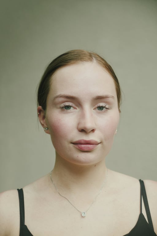 Minimal close portrait with neutral backdrop highlighting natural skin texture and calm expression.