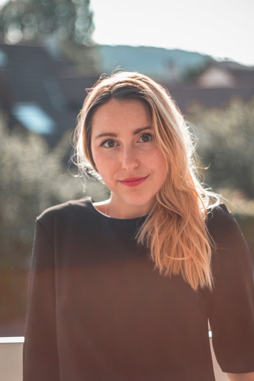 Outdoor portrait with soft sunlight, blonde hair, black top, gentle expression and warm background blur.
