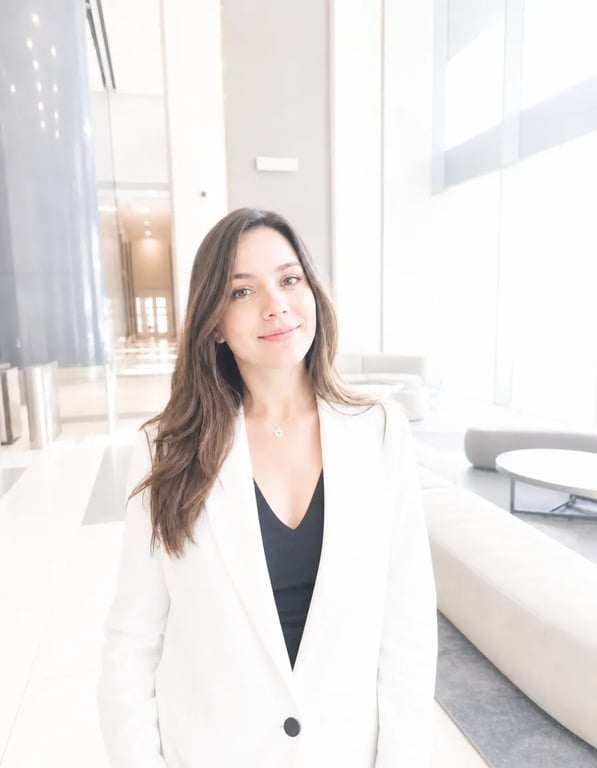 A young woman with long brown hair wearing a brilliantly glowing white blazer, standing in a washed-out overexposed bright lobby interior, high key photography style with pure white light flooding the scene, luminous porcelain skin, dreamy clean editorial fashion portrait feel.
