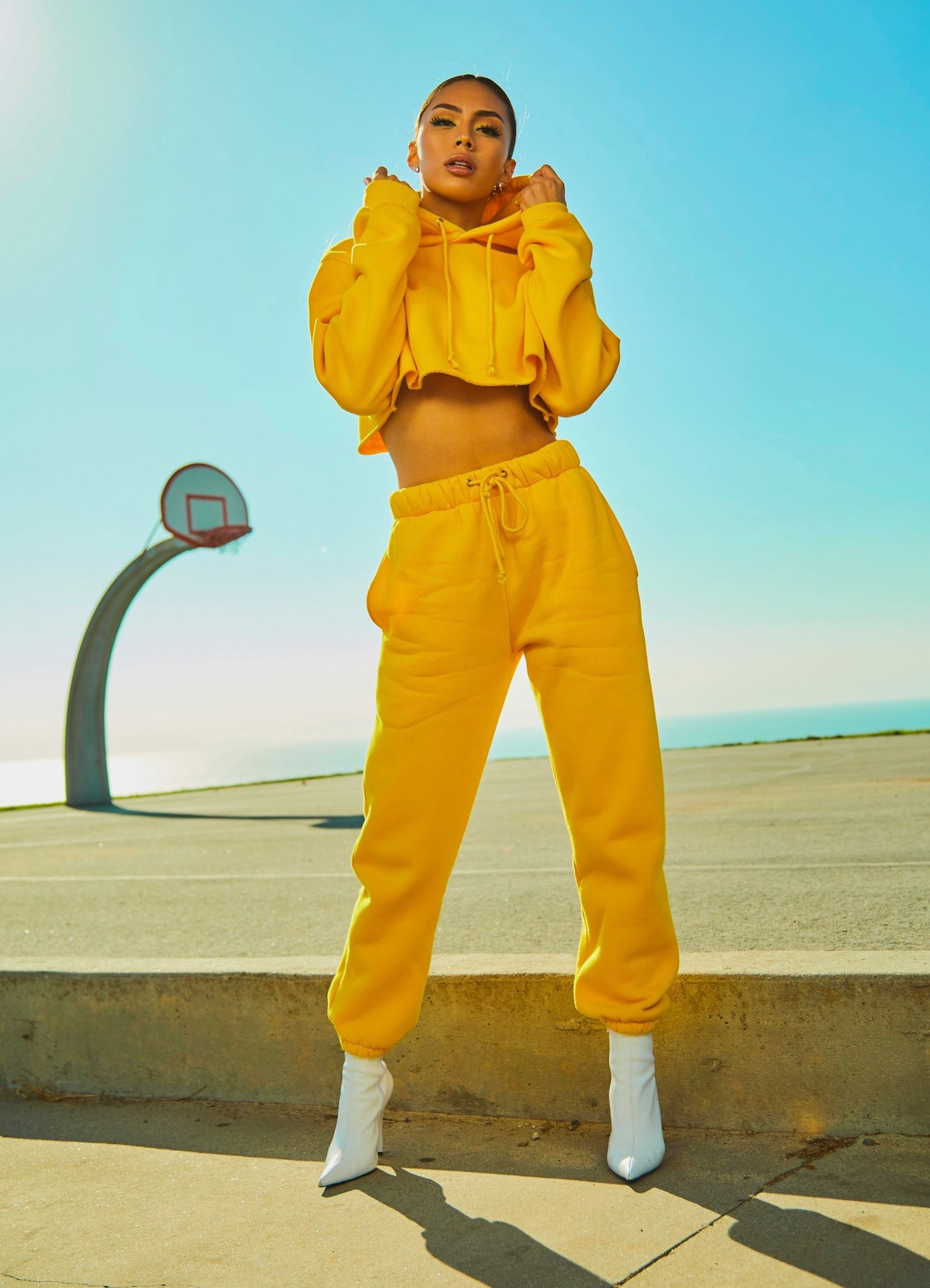 A woman in a bright yellow tracksuit posing outdoors under clear sky.
