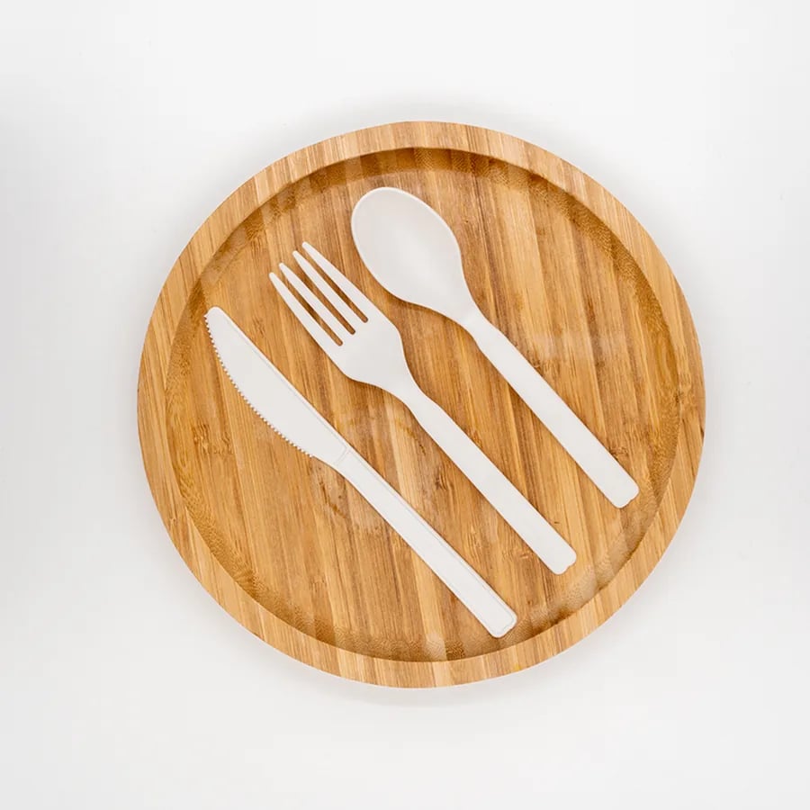 White CPLA knife, fork, and spoon arranged on a bamboo plate