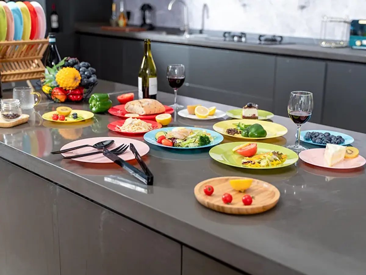 A full foodservice table arranged with disposable plates, cups, cutlery, and prepared dishes