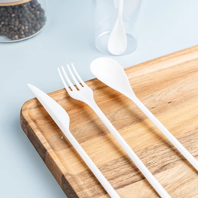 White CPLA knife, fork, and spoon arranged on a wooden board