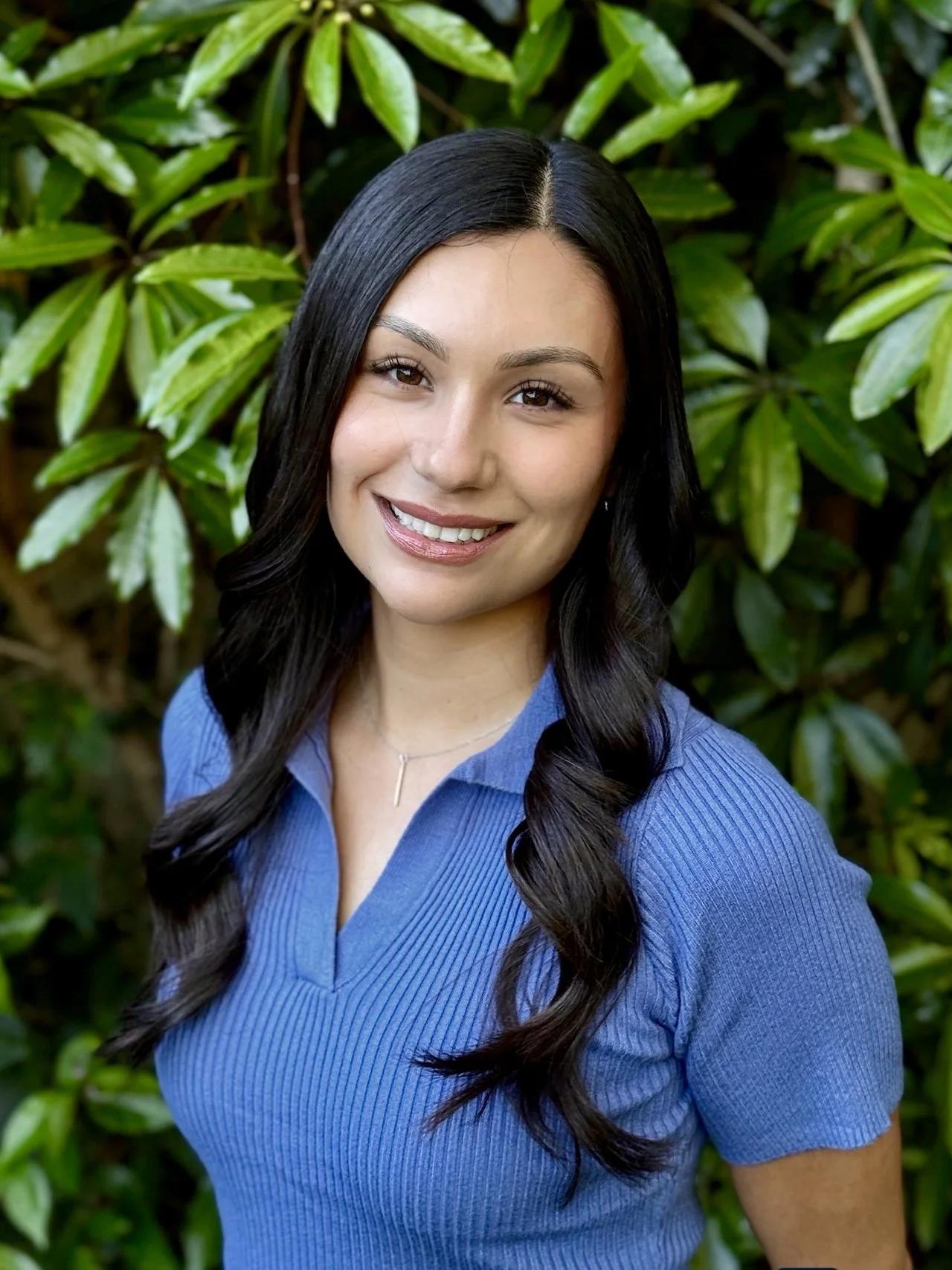 Jazmin Alarcon, LCSW, smiling in a blue top in front of green leaves