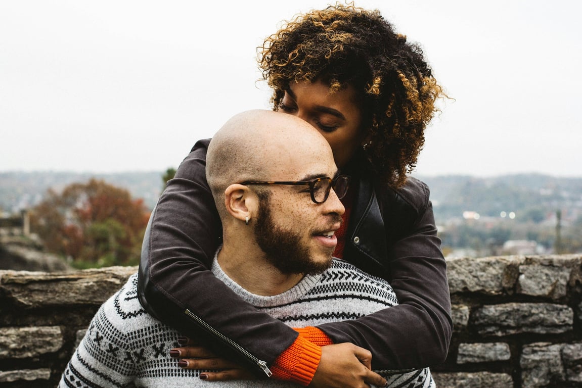 Two people embracing outdoors with a city skyline behind them
