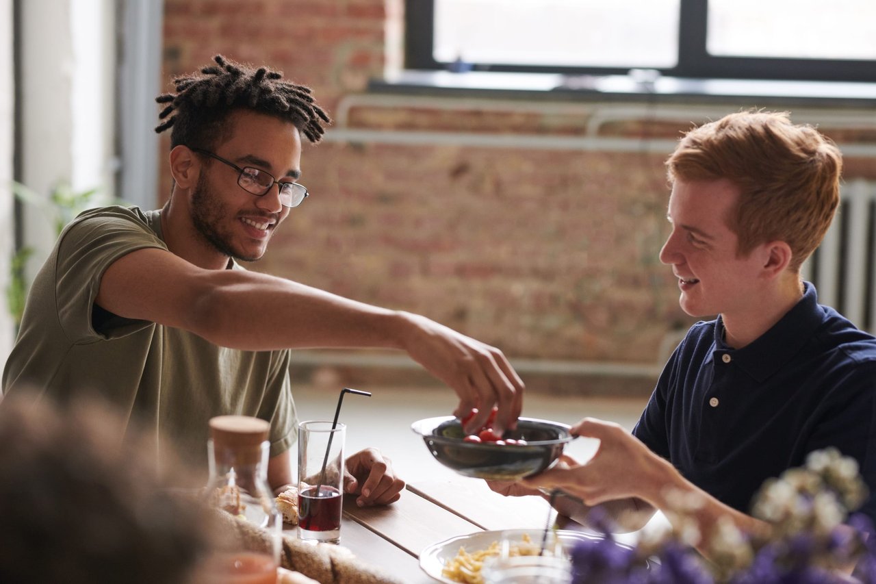 Two young friends laughing and sharing a dish at a sunlit table