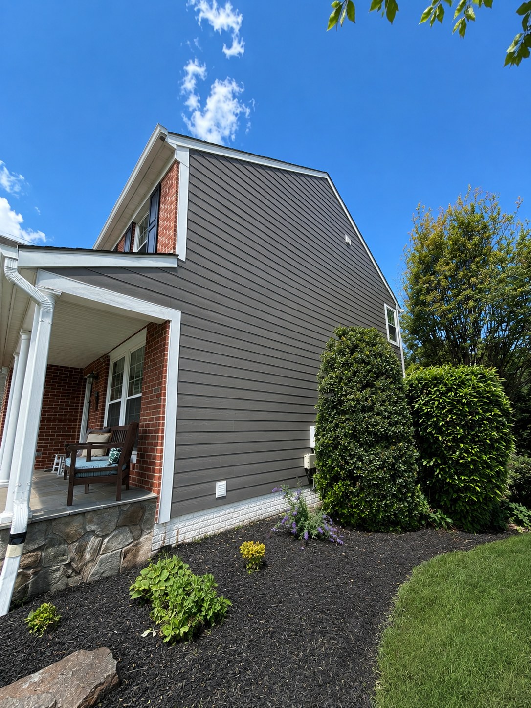 Gray lap siding and white trim on a gambrel-roof home with red brick and a covered front porch