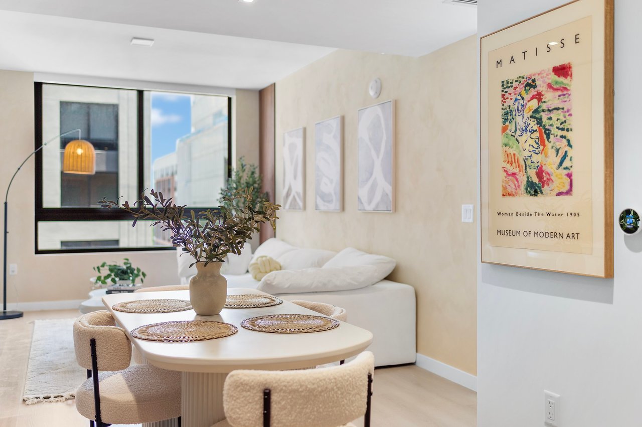 Modern living room with a dining table for four, a white sofa, artwork and large windows