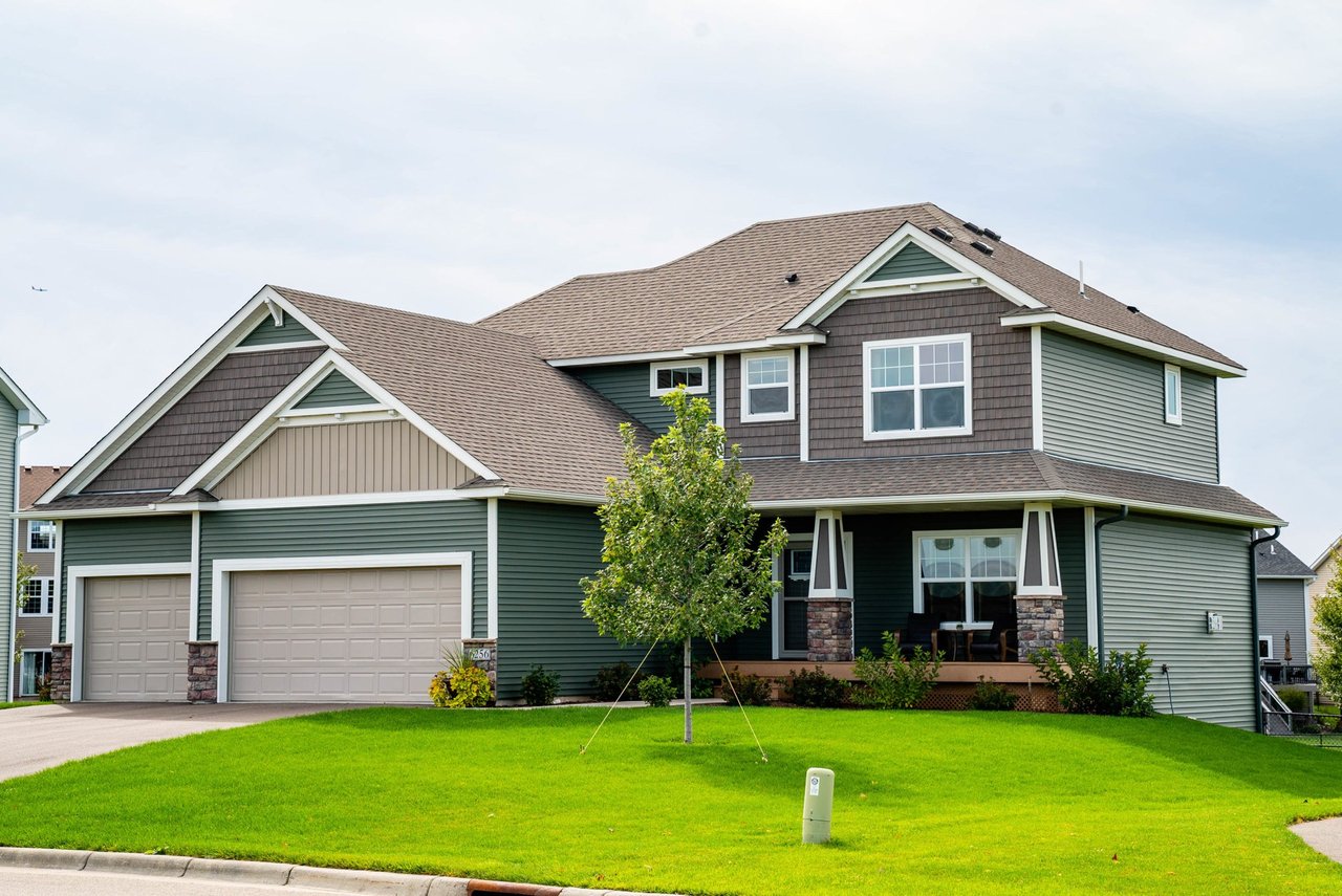 Deep green lap siding with shake accents, stone porch columns and white trim
