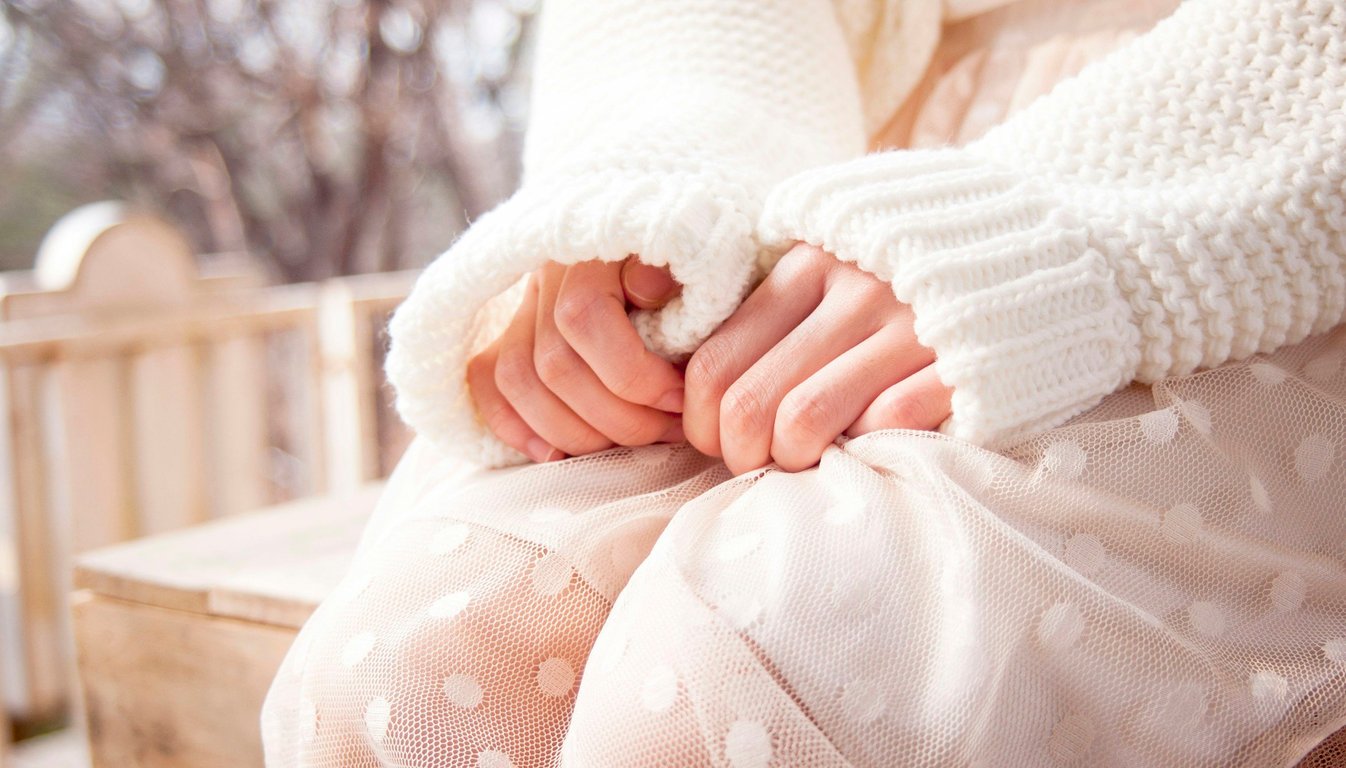 Hands held together in the shape of a heart over a soft pink sweater