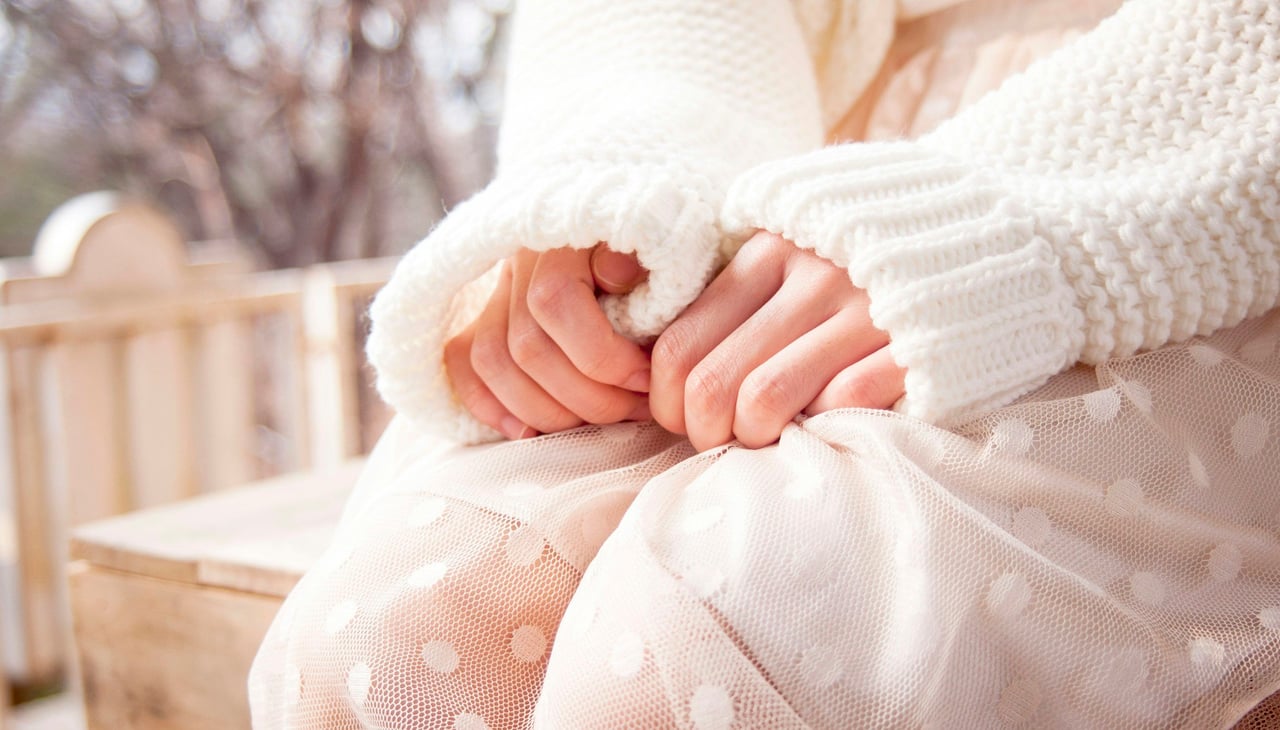Hands held together in the shape of a heart over a soft pink sweater