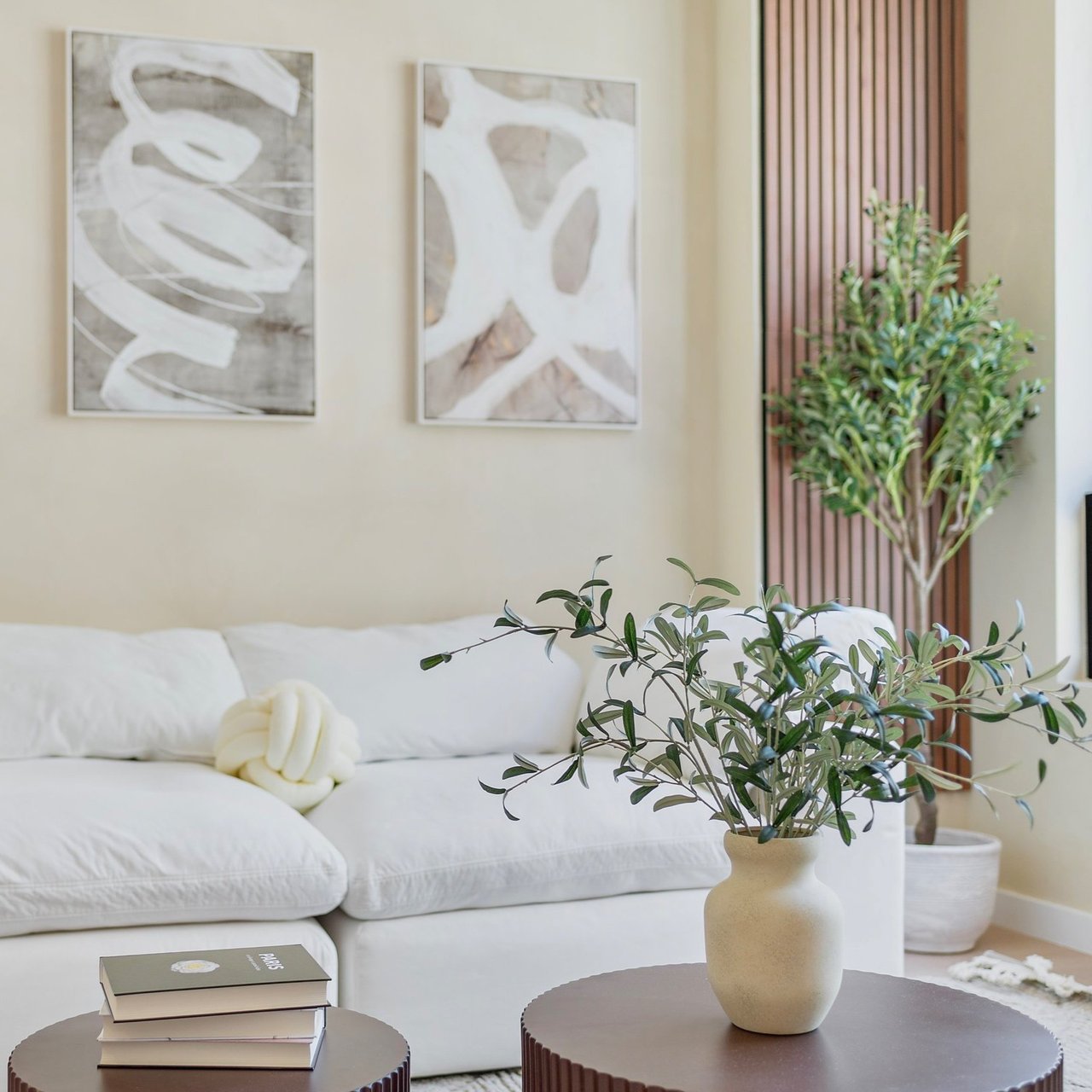 Cozy living room with a white sofa, black coffee table, green potted plants and abstract art