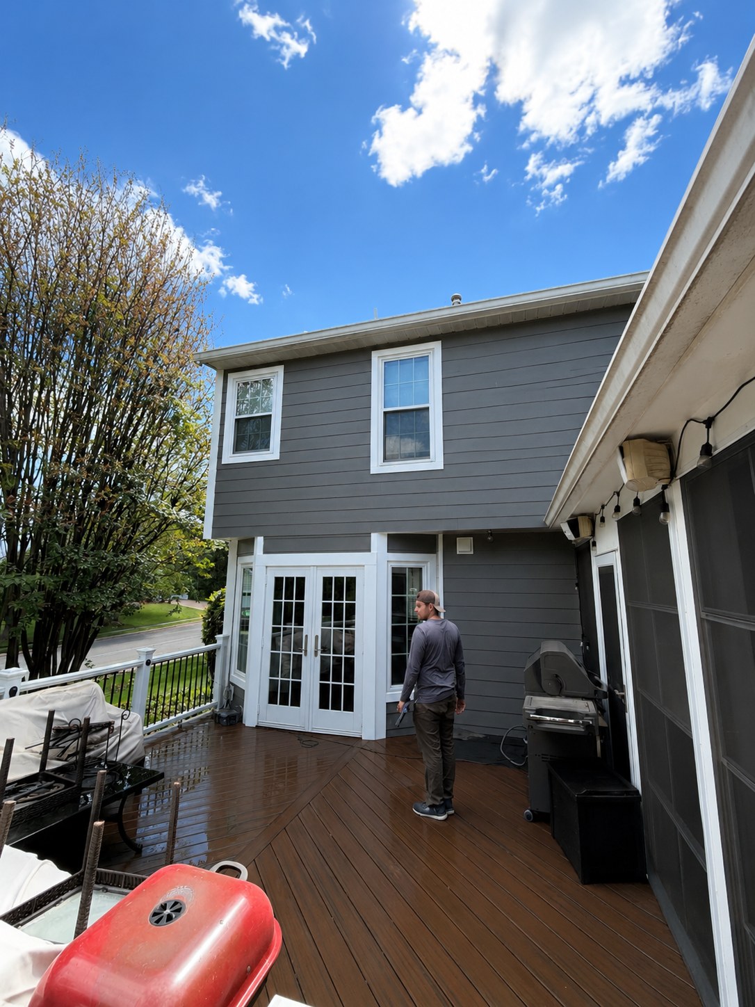 DMV Exteriors & Restorations crew member installing gray lap siding on a rear elevation above a composite deck