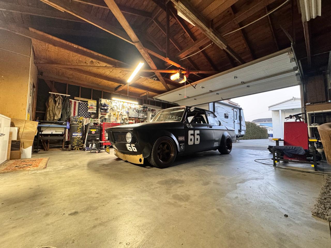 Black 1974 BMW 2002 race car, number 66, parked in a garage