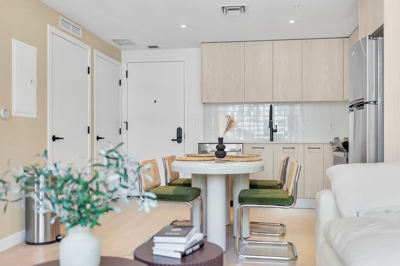 Kitchen and dining area with a round white table, green chairs and beige cabinetry