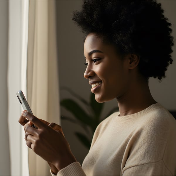 Mulher negra jovem com cabelo natural e expressão de leveza e alegria, usando o celular.