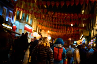 A group of people walk down a city street at night beneath a dense canopy of glowing red lanterns.
