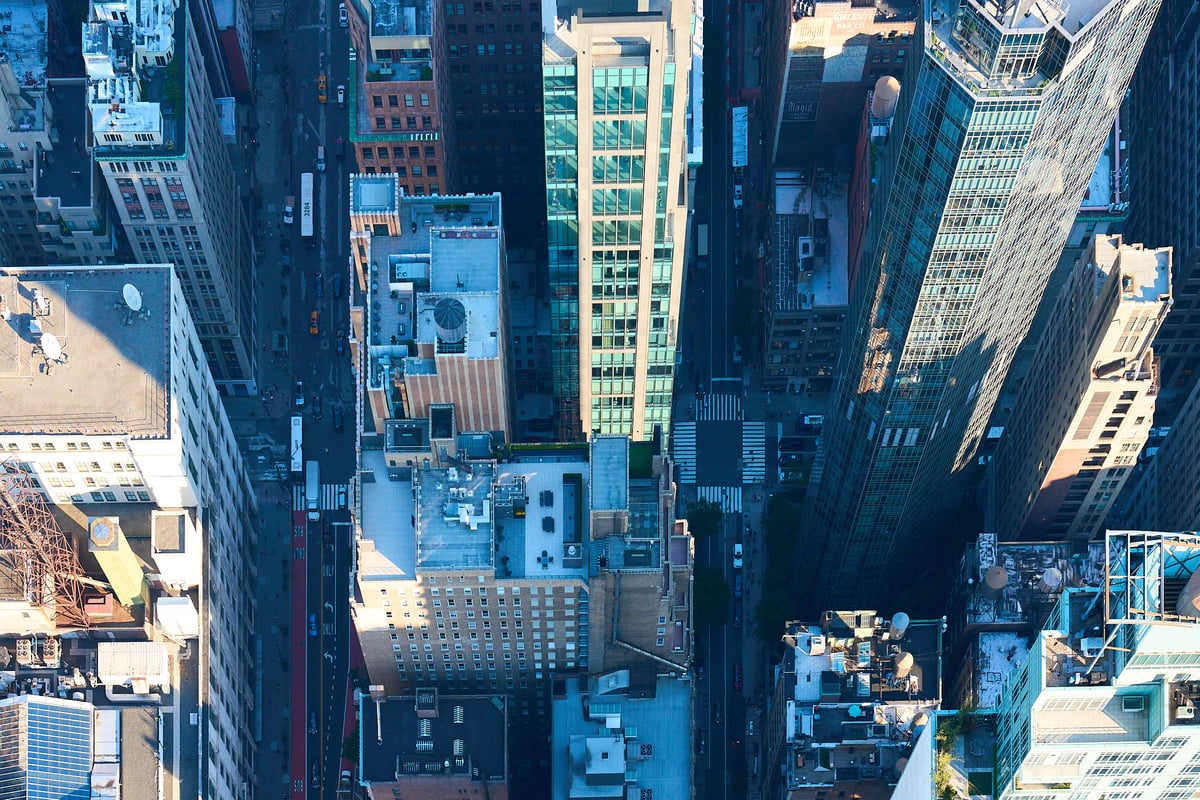 An aerial top-down view of dense city skyscrapers and streets with long shadows cast by the afternoon sun.