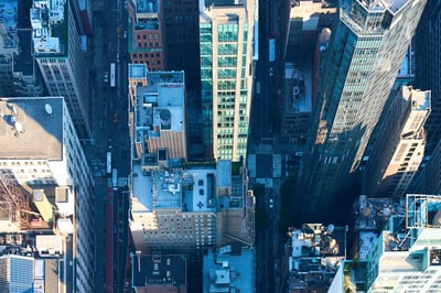 An aerial top-down view of dense city skyscrapers and streets with long shadows cast by the afternoon sun.