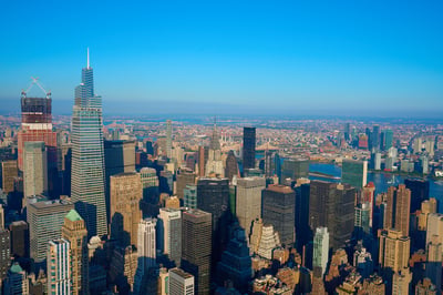 A high-angle aerial view of the Midtown Manhattan skyline featuring One Vanderbilt and the Chrysler Building under a clear blue sky with long afternoon shadows.