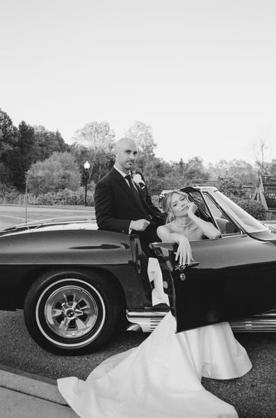 Bride leaning elegantly out of the Corvette door while groom stands tall beside her at dusk