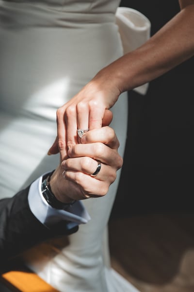 Close-up of the couple's hands interlocked — bride's engagement ring and pearl bracelet visible alongside groom's wedding band and watch