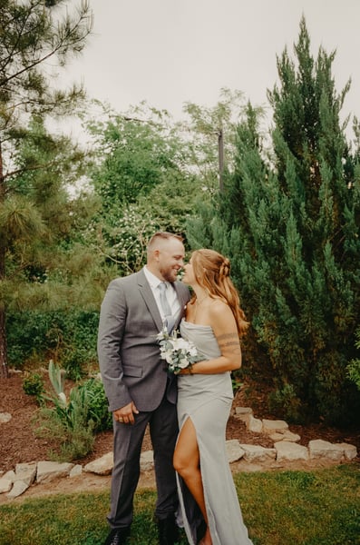 Couple laughing together in the garden, man in gray suit and woman in blue bridesmaid dress holding a bouquet