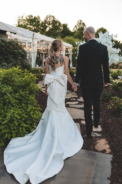Bride from behind on the dance floor in her white mini dress and oversized blazer, bejeweled Converse on full display, arms outstretched mid-dance as family members look on