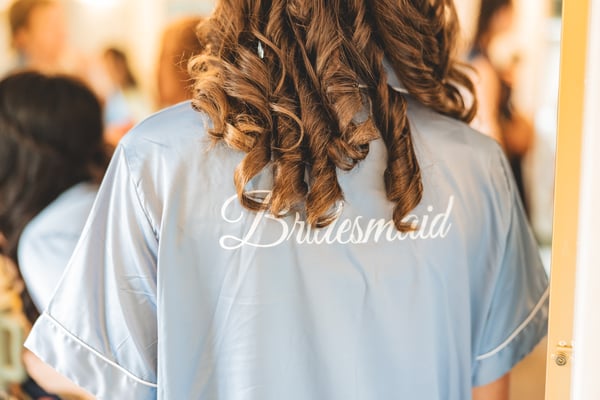 Bridesmaid in a pale blue satin robe with Bridesmaid script on the back, her curled brown hair flowing over her shoulders