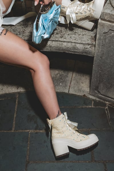 Detail of the bride's bejeweled Converse shoes and lower legs on the stone gazebo steps at night, blue bag resting beside her