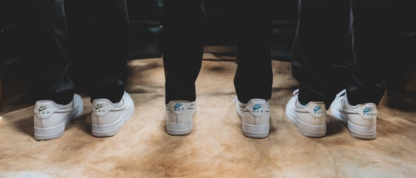 Three groomsmen standing side by side in dark suits showing the backs of their matching white Nike Air Force 1 sneakers
