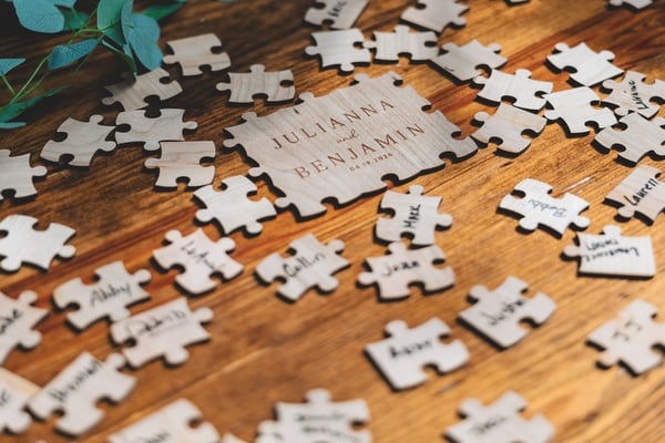 Wooden jigsaw puzzle guest book with Julianna and Benjamin engraved on the center piece, surrounded by signed puzzle pieces from wedding guests